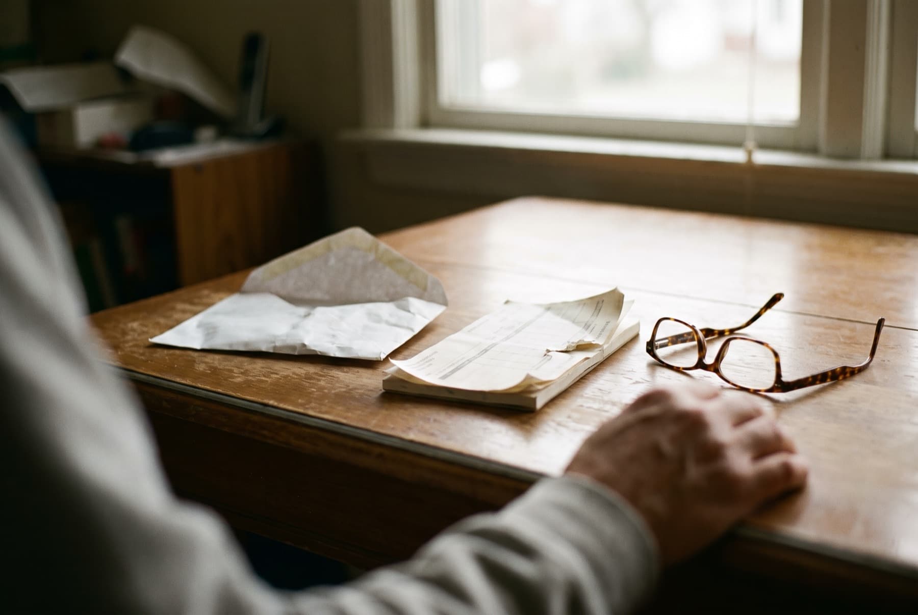 An empty open envelope and an opened bank deposit slip book on a table next to reading glasses