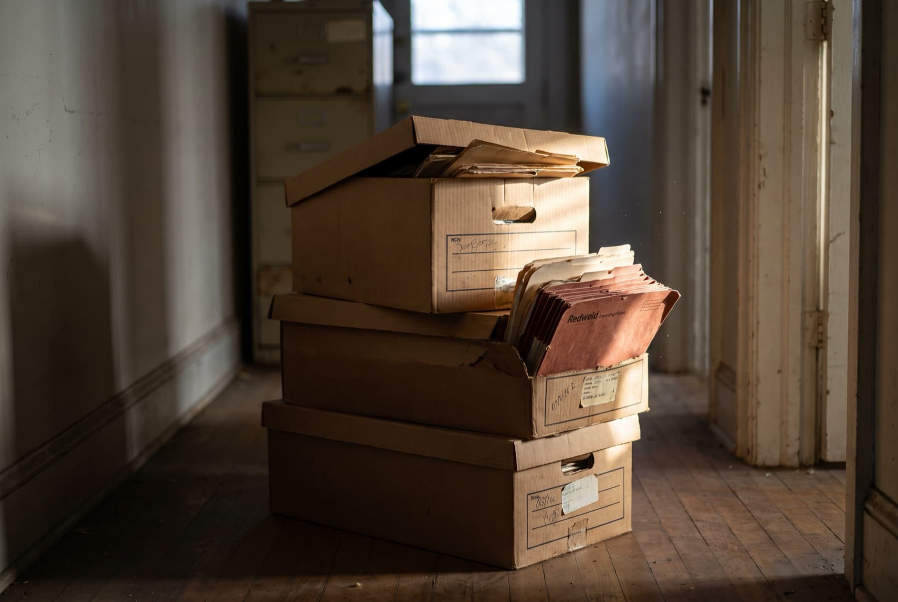Close view of three worn cardboard banker's boxes of client files stacked on the floor of a small law office hallway